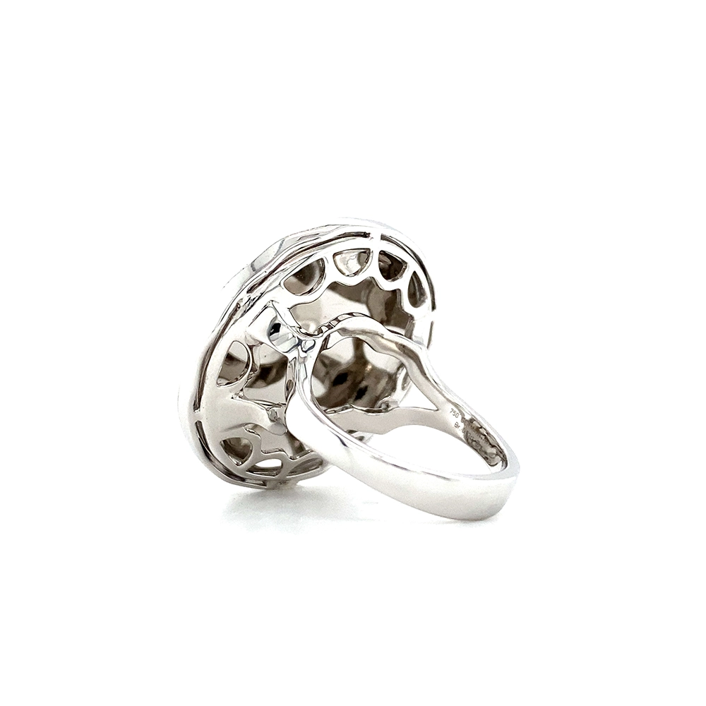 Ein Ring aus Weißgold mit einem runden Ringkopf. Dieser hat die Größe einer großen Münze. Die Oberfläche des Ringkopfes schimmert in einem kräftigen Rubinrot-Ton mit einem wellenartigen Muster. Darüber liegt die Form einer großen Blüte, besetzt mit vielen kleinen Diamanten.