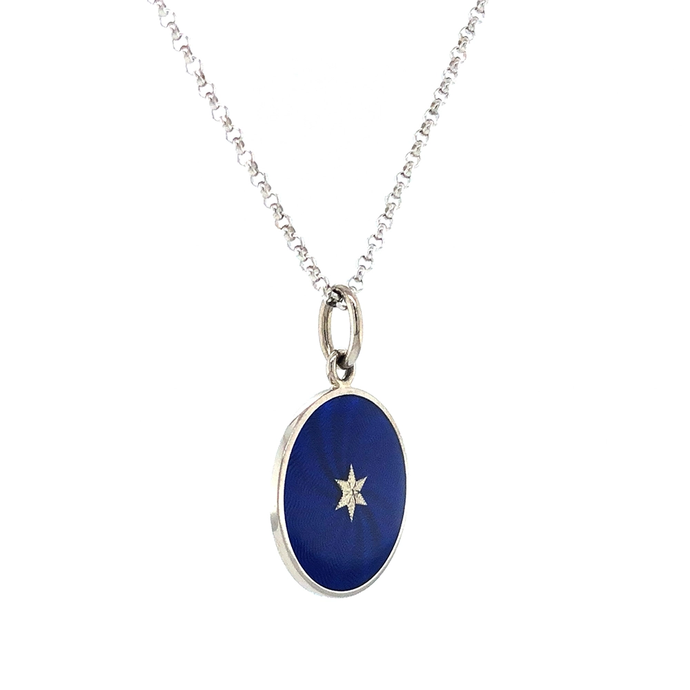Kleiner runder Anhänger aus Weißgold, etwa so groß wie eine kleine Münze. Die Vorderseite schimmert in transluzider Electric blue Emaille mit feinem Wellenmuster. In der Mitte liegt ein winziges sechseckiges Goldplättchen in Sternform mit mikroskopisch feinen Reliefdetails.