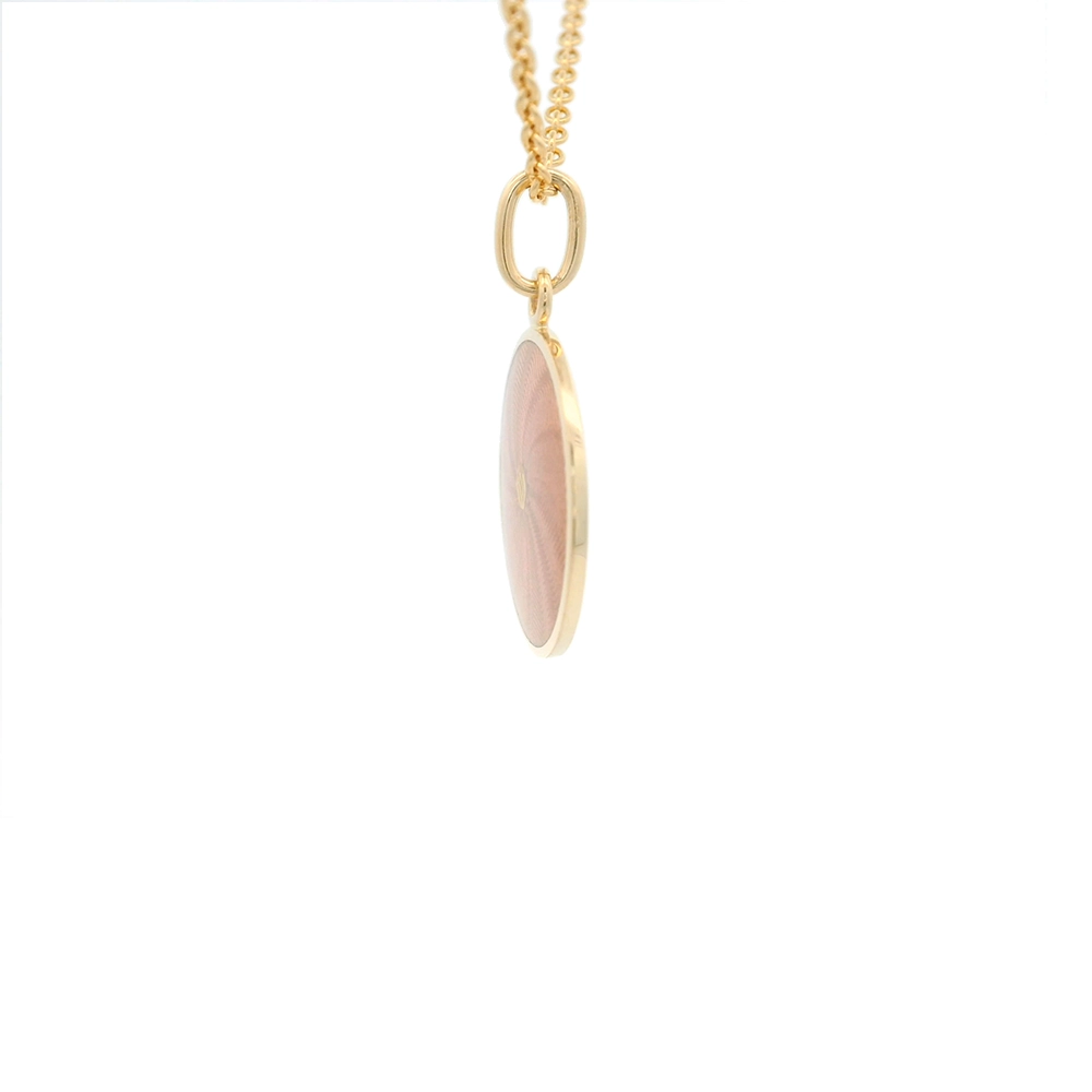 Kleiner runder Anhänger aus Gelbgold, etwa so groß wie eine kleine Münze. Die Vorderseite schimmert rosa in durchscheinender Emaille mit feinem Wellenmuster. In der Mitte ist ein winziges sechseckiges Goldplättchen eingelassen, das die Buchstaben V und M als Relief zeigt.